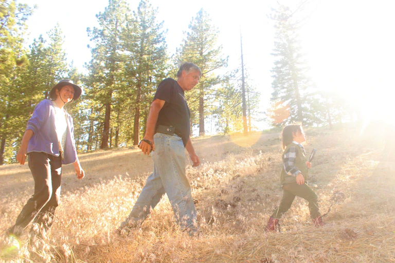 A grandchild walks across a tree-lined hill with grandparents in tow.