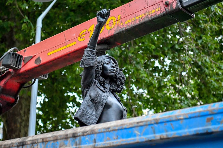 A sculpture of a woman protester rests in a waste skip, her fist in the air.