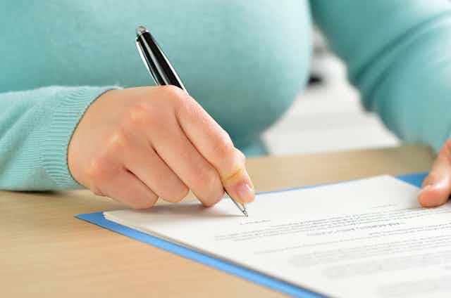 A woman signs a form with a pen. 
