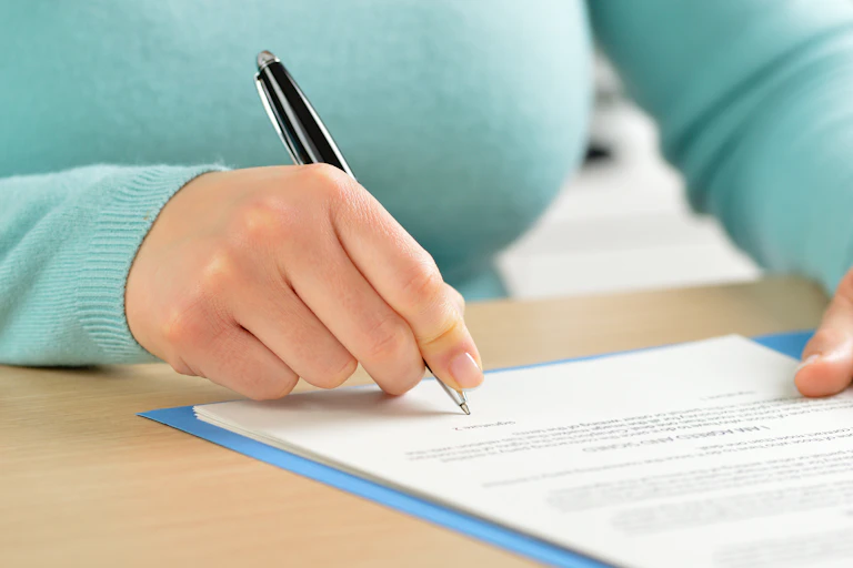 A woman signs a form with a pen.