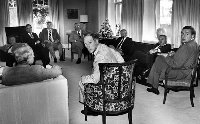 Pierre Trudeau turns in his seat to look at the camera as provincial premiers look on.
