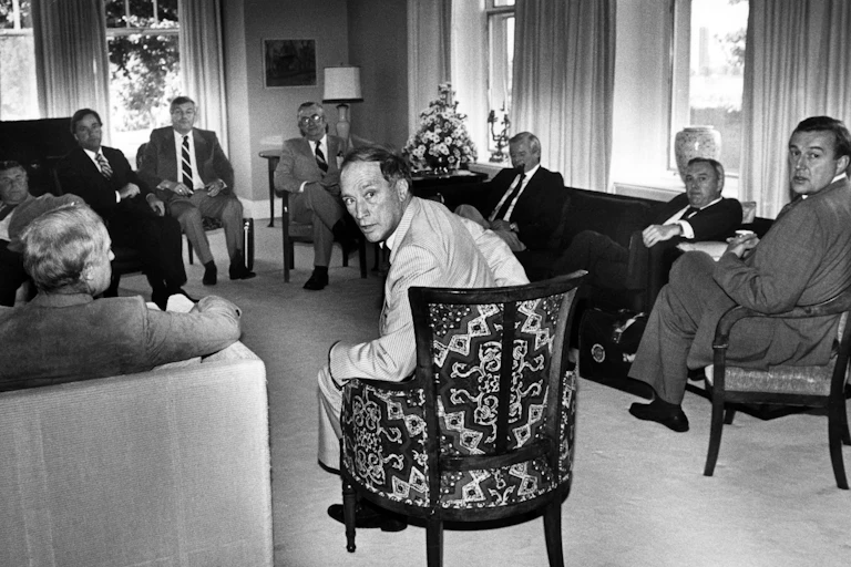 Pierre Trudeau turns in his seat to look at the camera as provincial premiers look on.