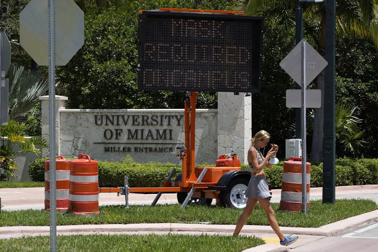 A female student walks in front of a sign at the University of Miami in Coral Gables, Fla.