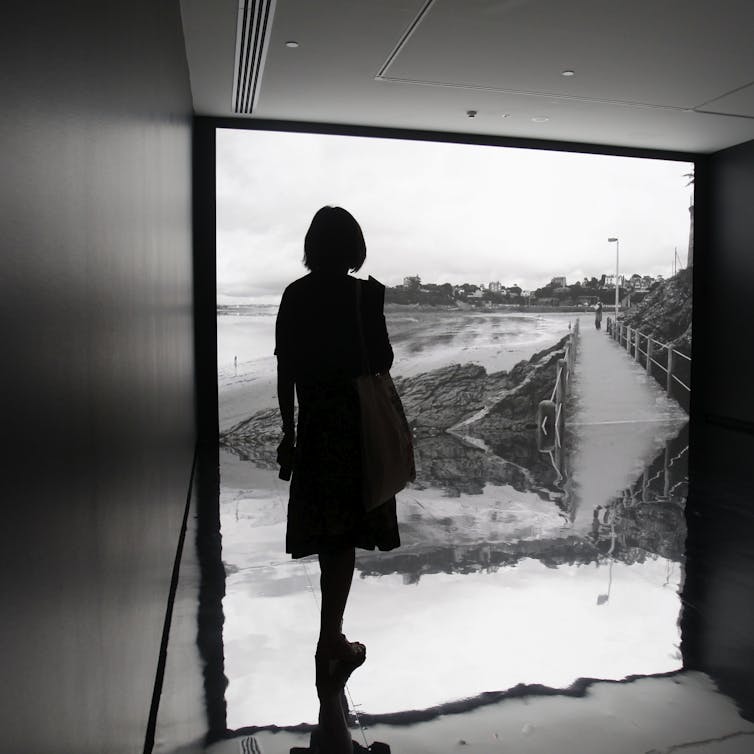 Woman in silhouette stands in front of a grey-scale video.