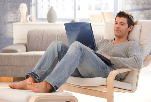 Man sitting in armchair looking at open laptop on his lap
