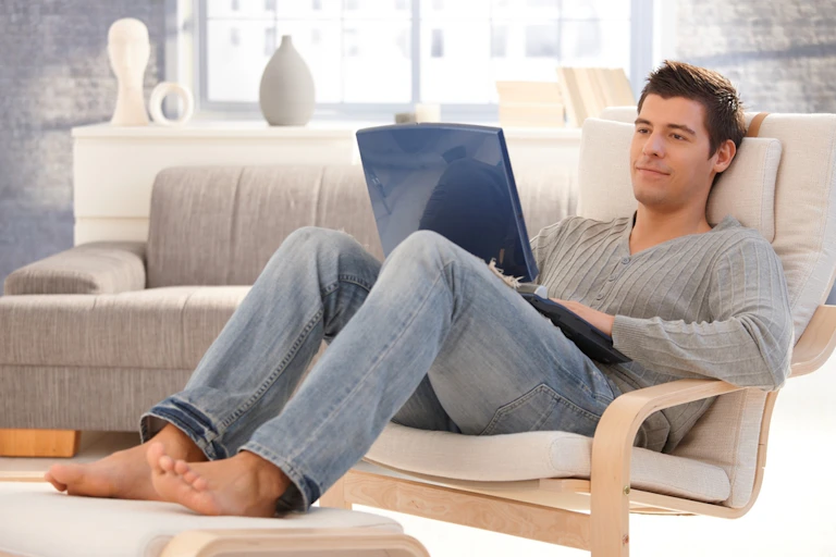 Man sitting in armchair looking at open laptop on his lap