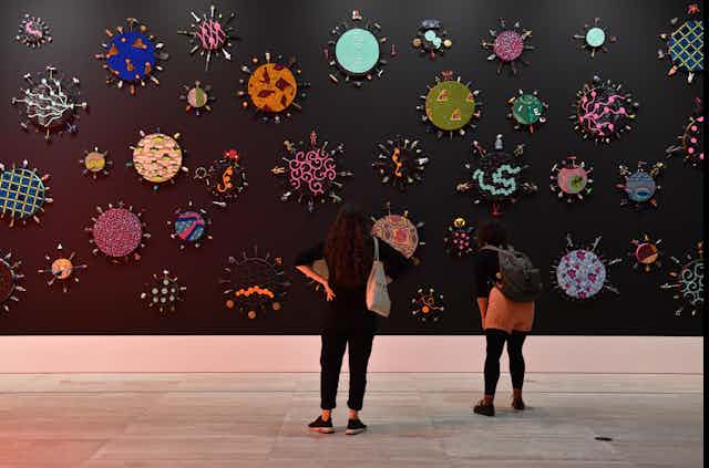 Two women stand in a gallery, looking at colourful shapes