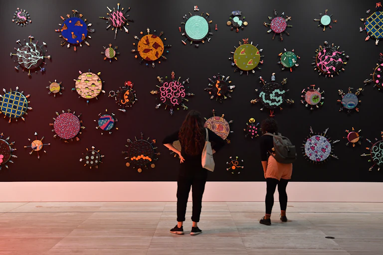 Two women stand in a gallery, looking at colourful shapes