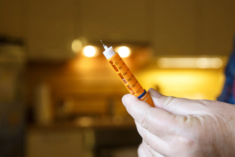 A hand holds an insulin injection.