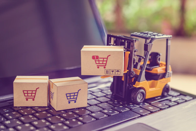 Una carretilla de juguete sobre un teclado de ordenador transporta paquetes ilustrados con carritos de la compra.