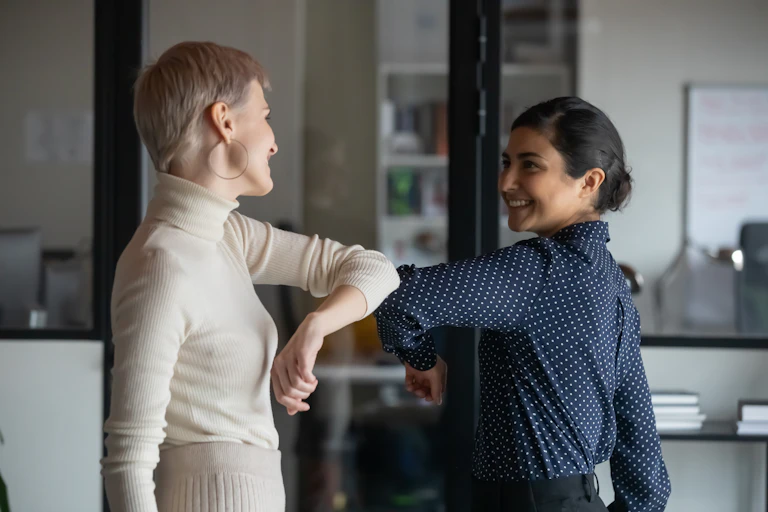 Two women touch elbows in the office.