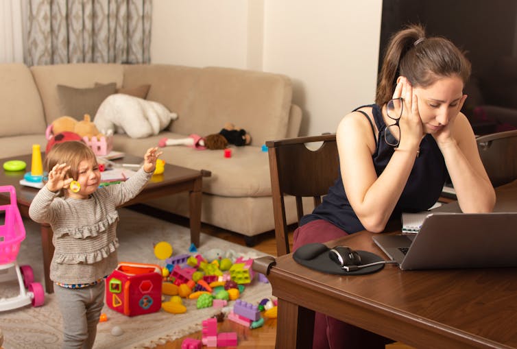 Mother hunched over laptop, with small child crying.