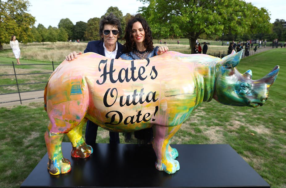 Ageing rock star plus wife pose behind psychedelic rhino.