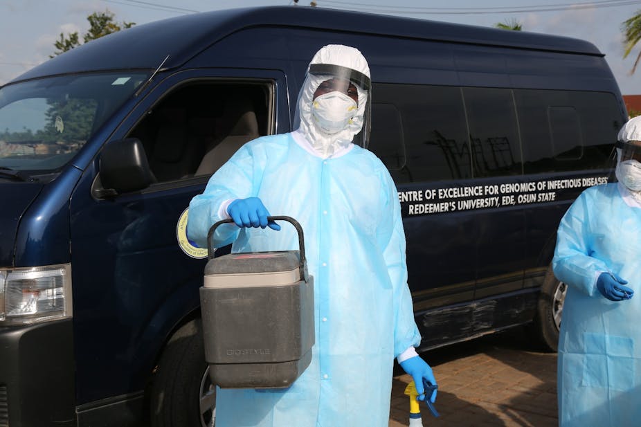 People wearing protective gear and carrying a cooler container in front of a vehicle from the African Center of Excellence for Genomics of Infectious Disease in Nigeria