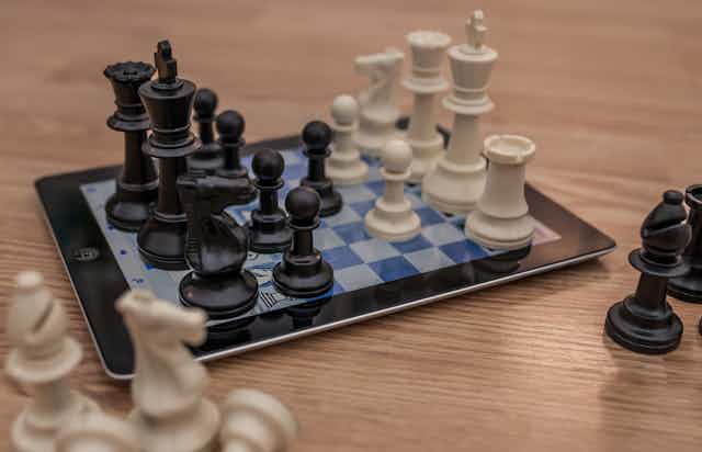Chess pieces sitting on an iPad displaying a chess board.