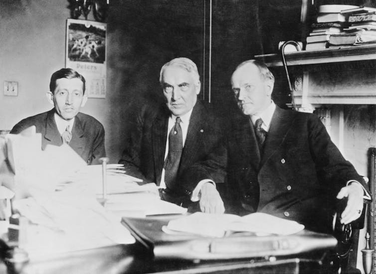 Three men at a table stacked with papers
