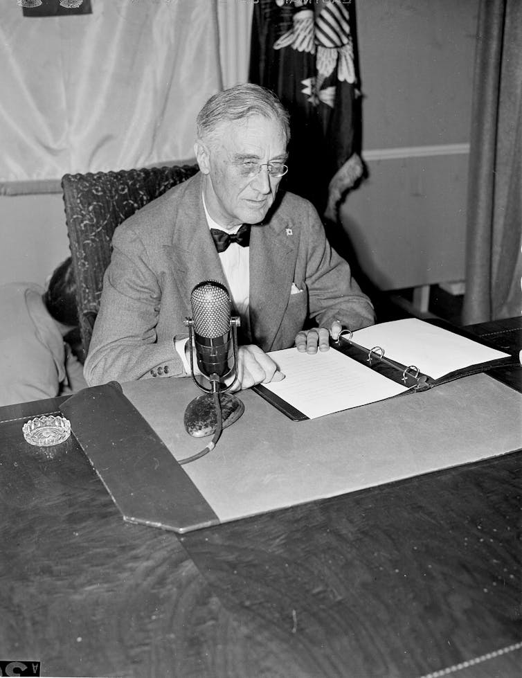 Franklin Roosevelt at a desk with a paper and a microphone