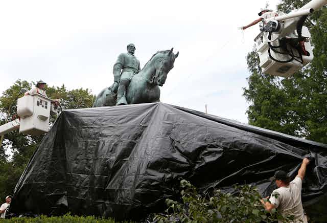 Workers use cranes to drag a black tarp over the bronze Lee statue.