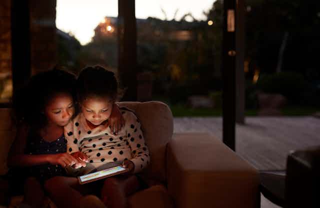 Two young girls using a digital tablet, at night