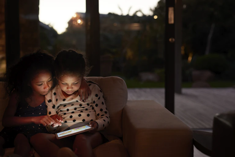 Two young girls using a digital tablet, at night