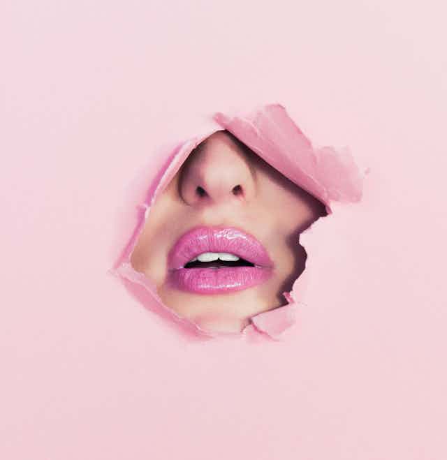 Pink lips and a nose peak through torn pink paper