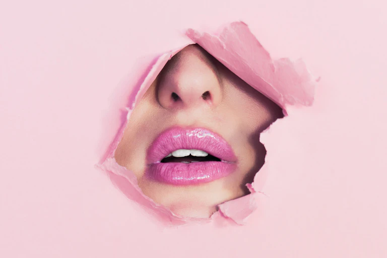 Pink lips and a nose peak through torn pink paper