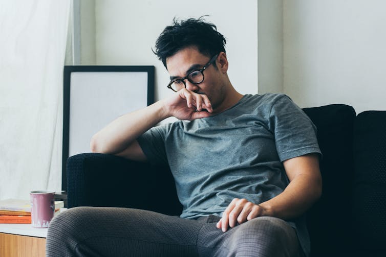 Young man sits on couch, thinking.