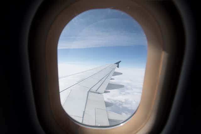 The wing of an airplane is seen above the clouds through an aircraft window.
