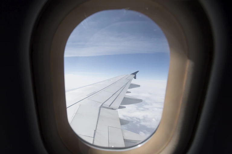 The wing of an airplane is seen above the clouds through an aircraft window.