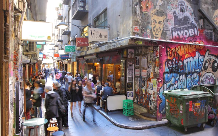 People moving through a laneway in Melbourne with cafes on each side.