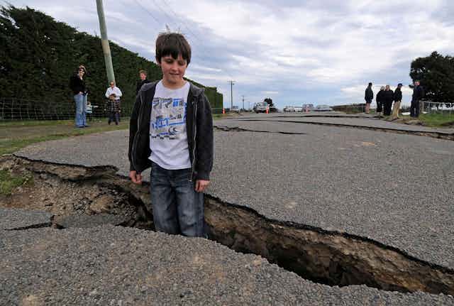 A young boy stands inside a crack in a road that was caused by an earthquake.