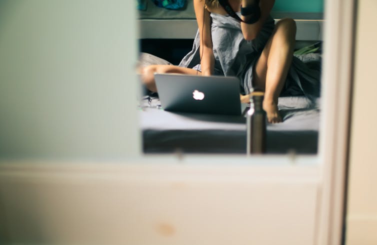 A woman types on a laptop while wrapped in a sheet.