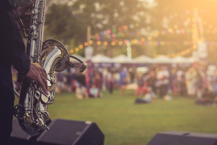 Man plays saxophone to outdoor audience.