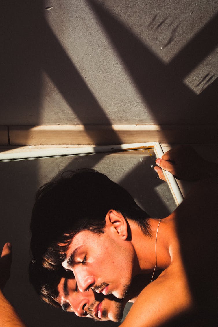 A man leans against his reflection in a mirror.