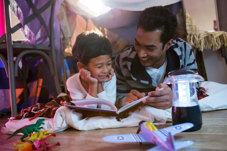 A father and son read in a blanket fort.