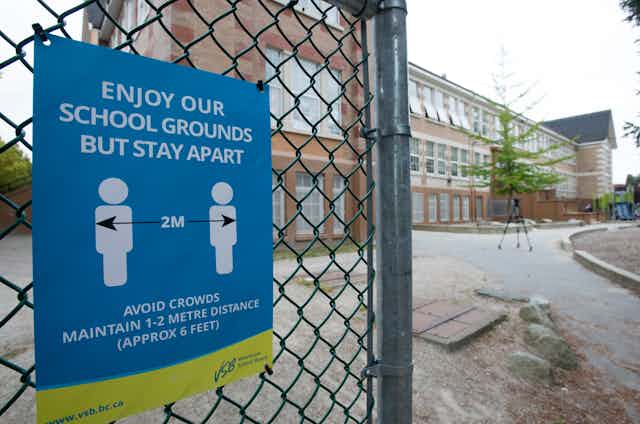 A physical distancing sign seen on a fence by a school.