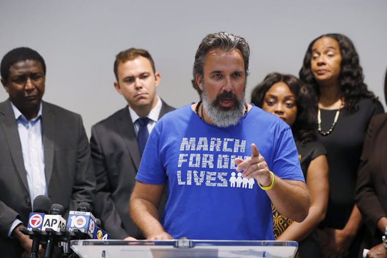 A bearded man wearing a March for Our Lives T-shirt gestures as he speaks.