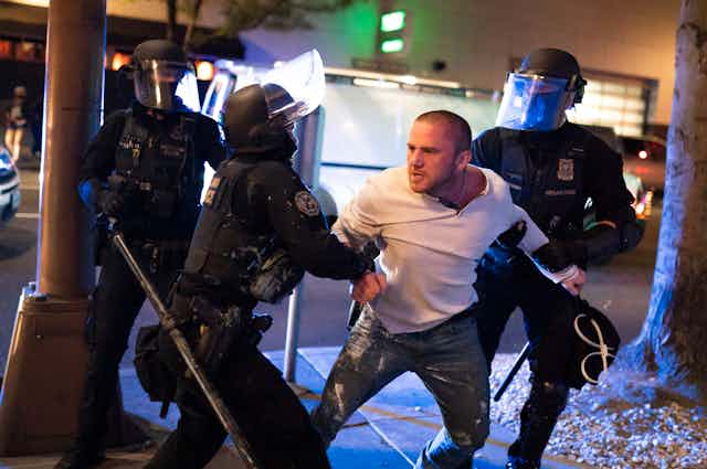 Police restrain a man in a white shirt