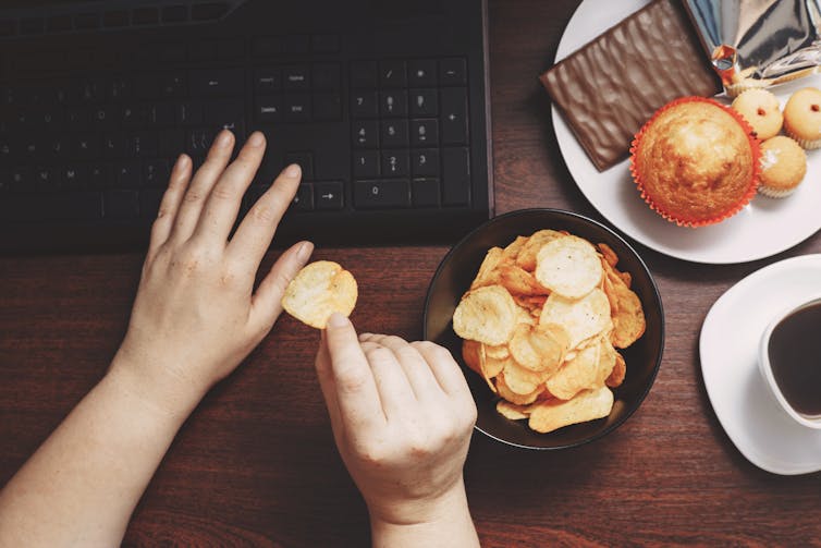 Person's hands typing on keyboard while eating unhealthy snacks.