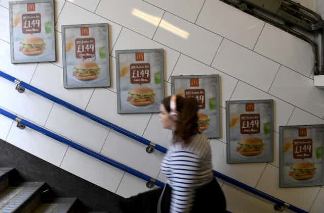 A commuter on London Underground walking past adverts selling a cheap burger