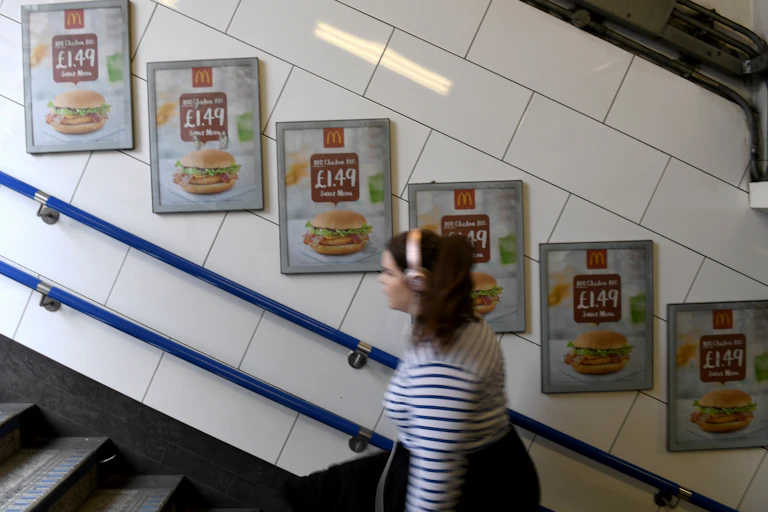 A commuter on London Underground walking past adverts selling a cheap burger