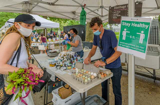 A shopper at a Brooklyn Greenmarket looks at a sign encouraging social distancing.