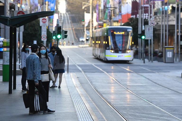 Two people wearing masks in Melbourne with passing tram