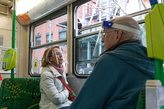 Two commuters on a Melbourne tram wearing face shields.