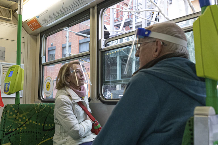 Two commuters on a Melbourne tram wearing face shields.