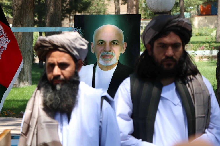Two Taliban stand in front of a poster of Afghan president Ashraf Ghani
