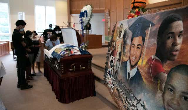 Mourners stand over the casket of 17-year-old Brandon Hendricks-Ellison while a photo montage of the 17-year-old is in the foreground.