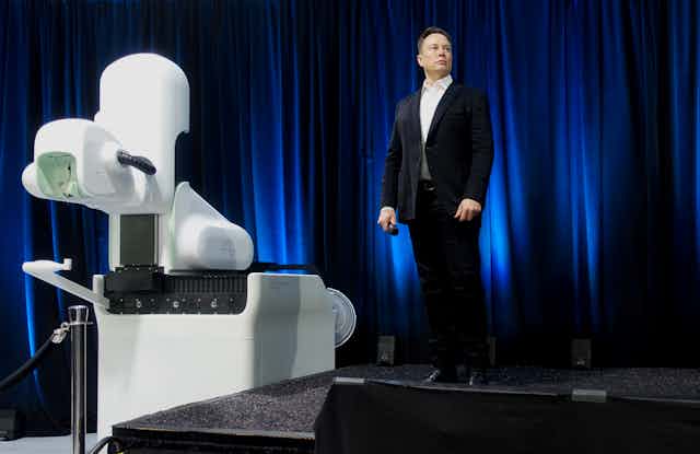 Picture of Elon Musk at Neuralink presentation with robot. 