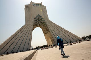 Donna che cammina verso un grande arco a Teheran.