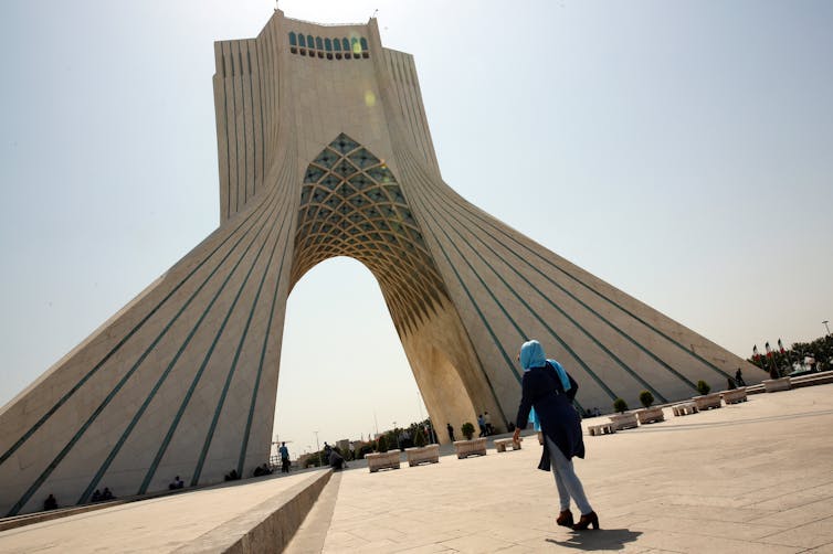 Woman walking towards large archway in Tehran.